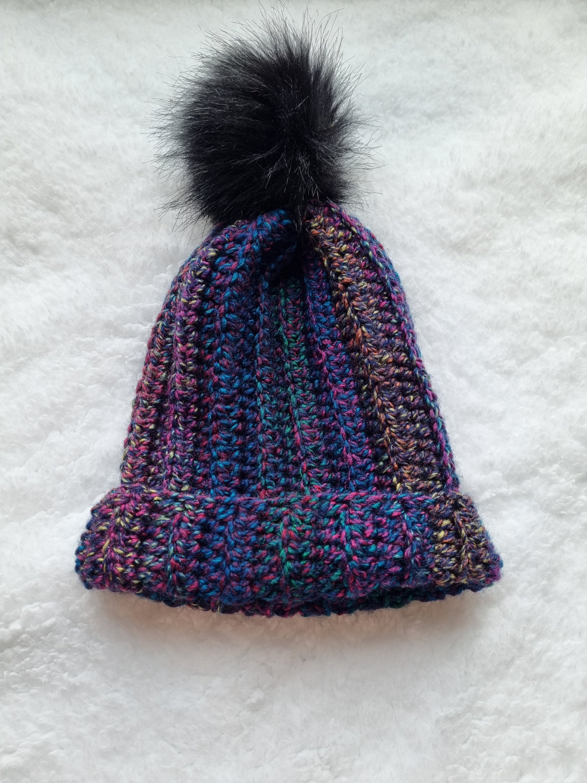 Multi-coloured flecked hat with black faux pompom.